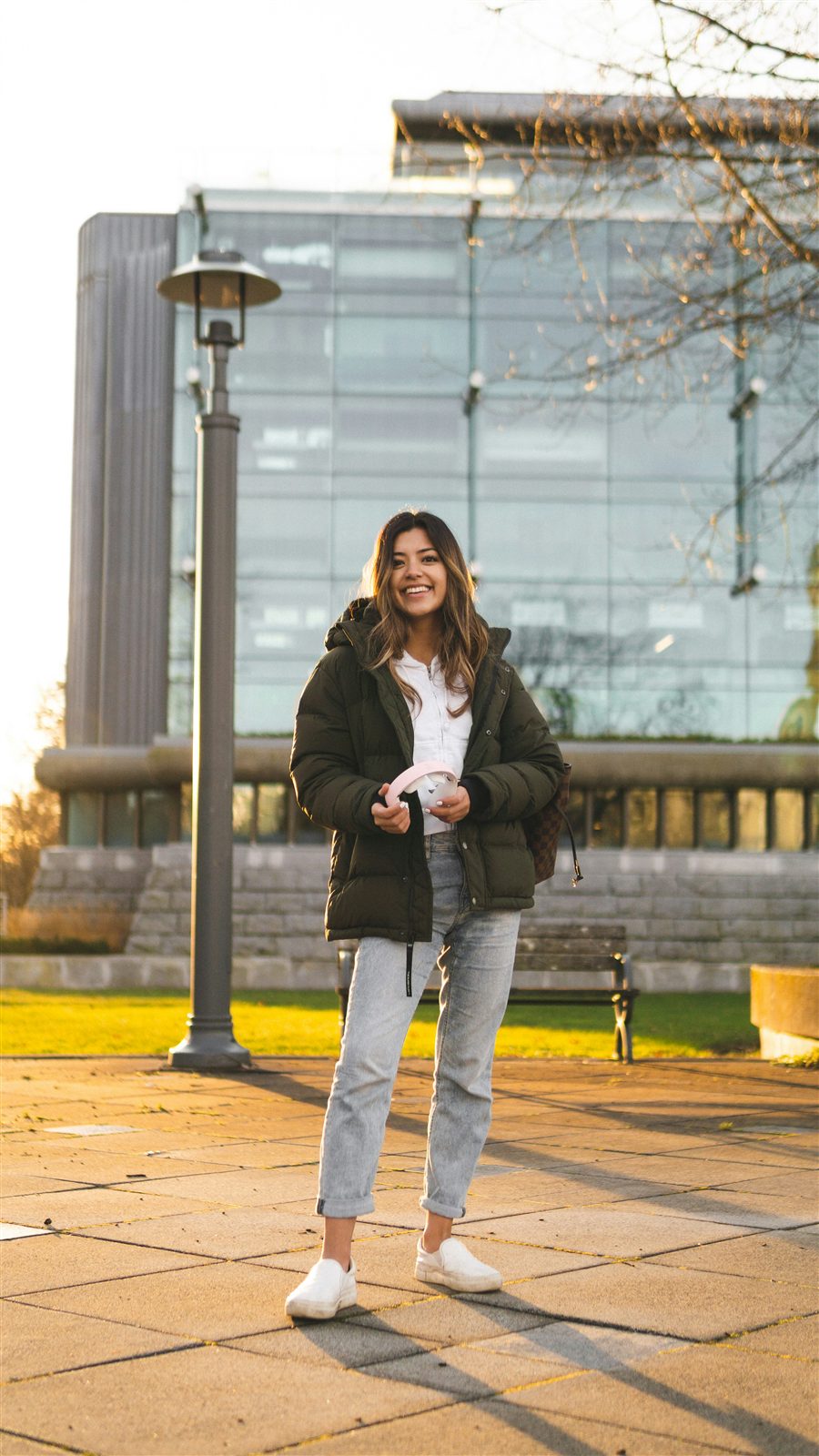 A student smiling on campus at golden hour, headphones in hand